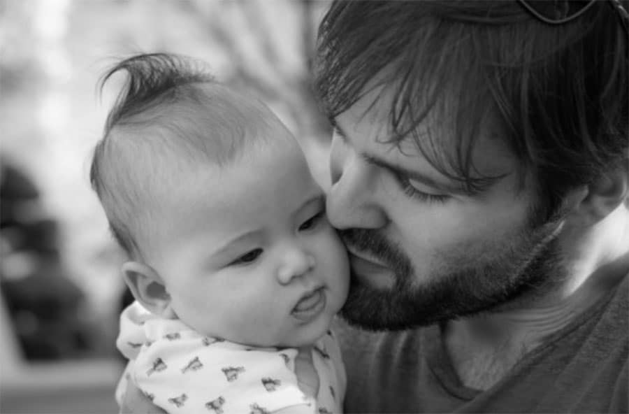 Un homme blottit affectueusement son bébé, qui regarde de côté, quelques instants avant un "Test de paternité".