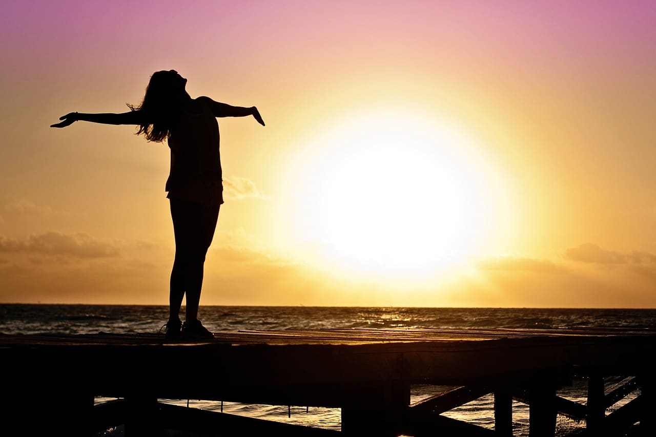 Figure silhouettée avec les bras tendus debout sur une jetée au coucher du soleil.