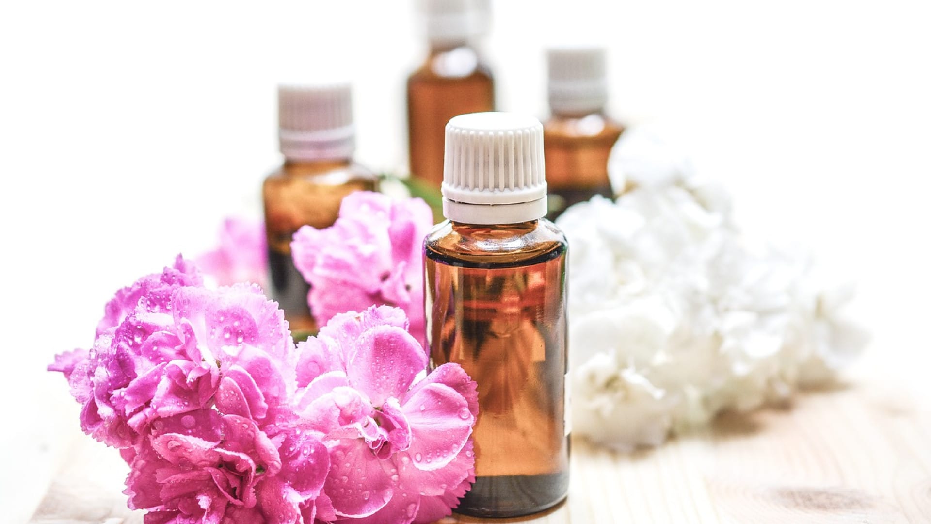Bouteilles d'huile essentielle avec fleurs roses et blanches fraîches sur une surface en bois.