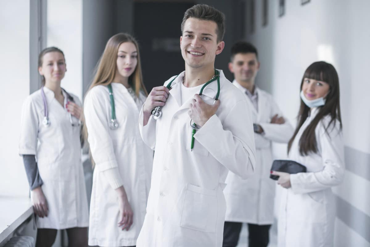 Un groupe de professionnels de la santé souriants debout dans un couloir, avec un médecin traitant au premier plan tenant un stéthoscope.