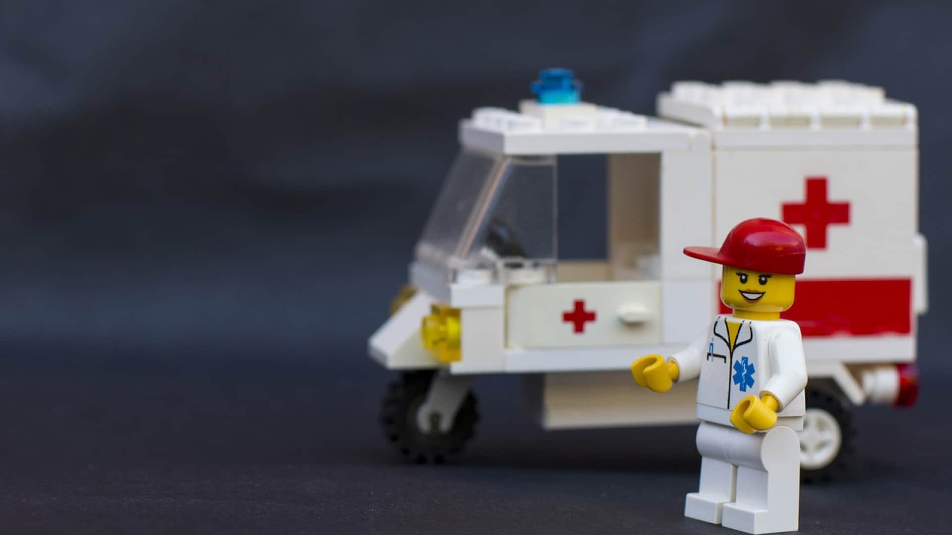 Une figurine d'ambulancier en Lego "Mission Santé" debout à côté d'une ambulance en Lego blanche avec des croix rouges dessus.