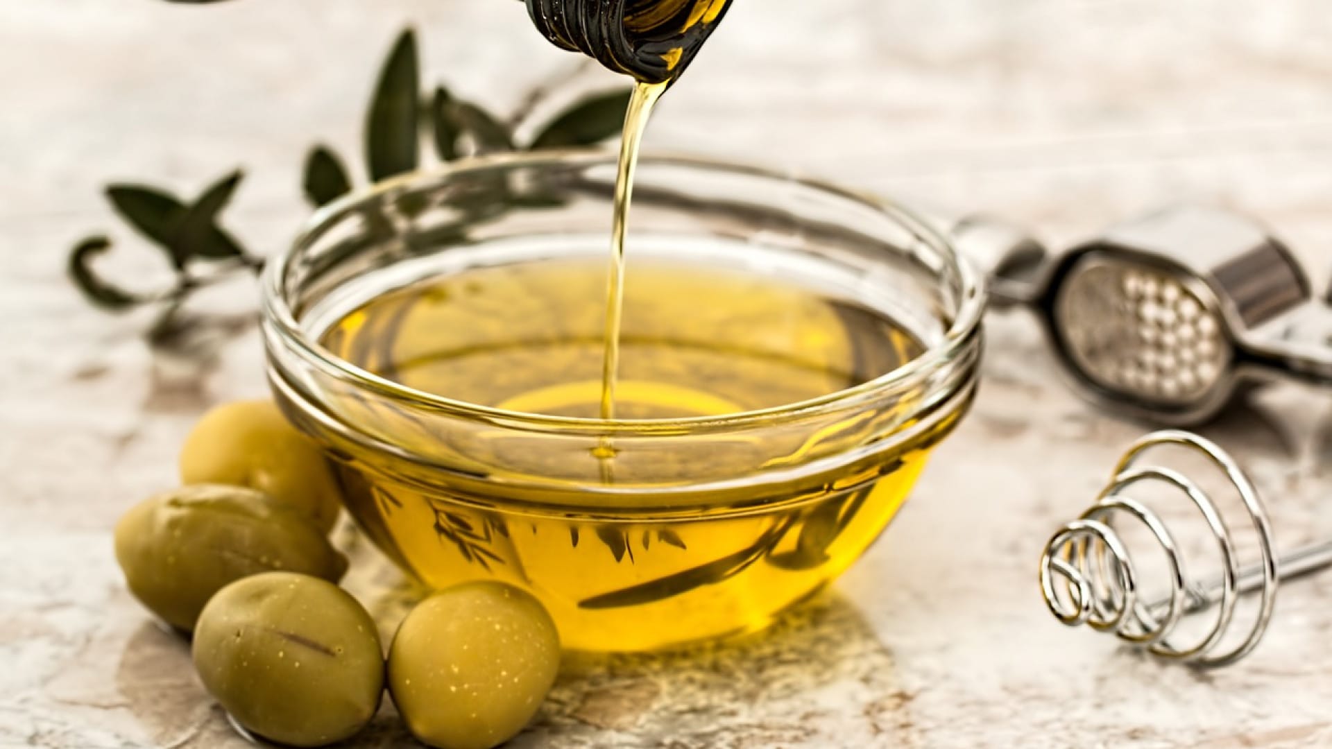 Verser l'huile d'olive dans un bol en verre avec des olives et des branches d'olivier sur le côté.