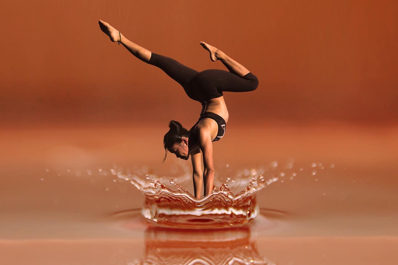 Femme effectuant un poirier avec les jambes fendues sur une surface d'eau réfléchissante, créant un effet d'entraînement.