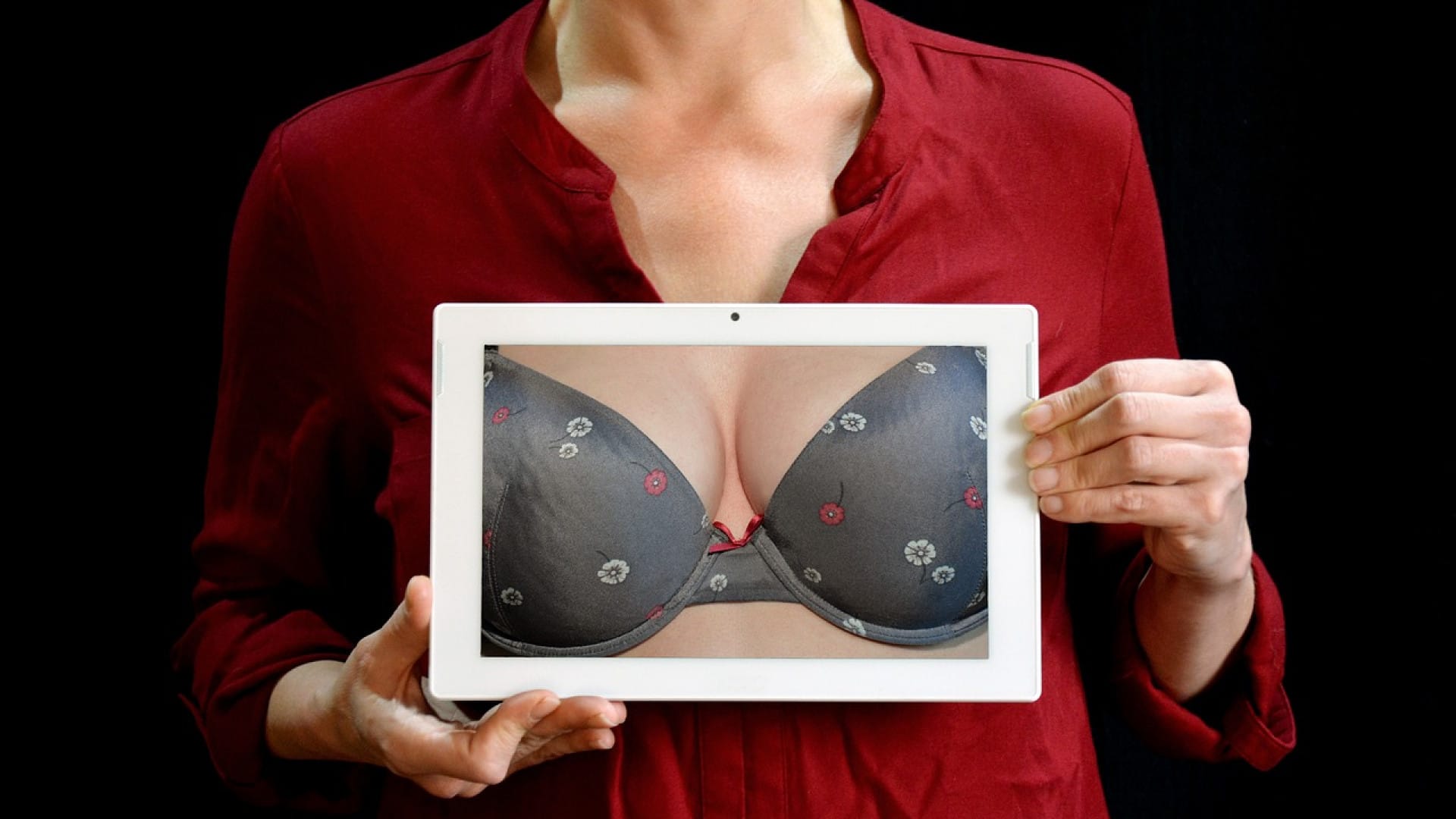 Personne tenant un comprimé avec l’image d’un soutien-gorge devant sa poitrine, se demandant « pour qui » est la chirurgie mammaire recommandée.