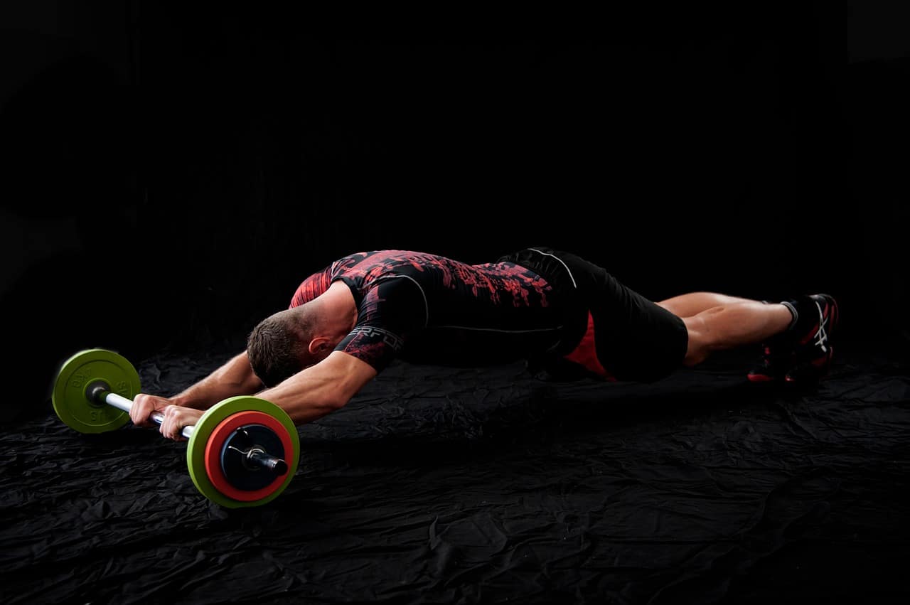 Homme effectuant un exercice avec une roue ab sur un tapis noir sur fond sombre.