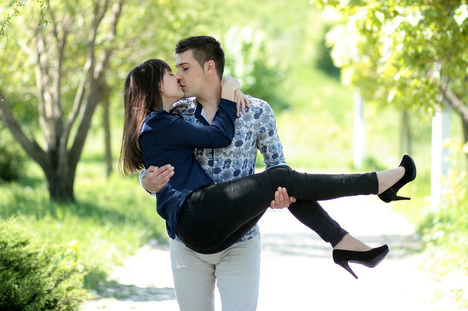 Homme tenant et embrassant une femme dans une allée de parc ensoleillée.