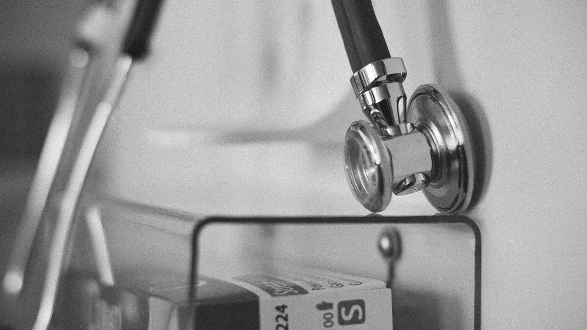 Photo en noir et blanc d'un stéthoscope posé sur une surface vitrée dans une clinique esthétique en Suisse, avec des fournitures médicales en arrière-plan.