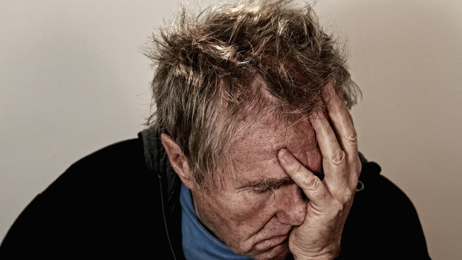 Un homme en détresse, tenant sa tête dans sa main, recherche un traitement pour sa douleur chronique.