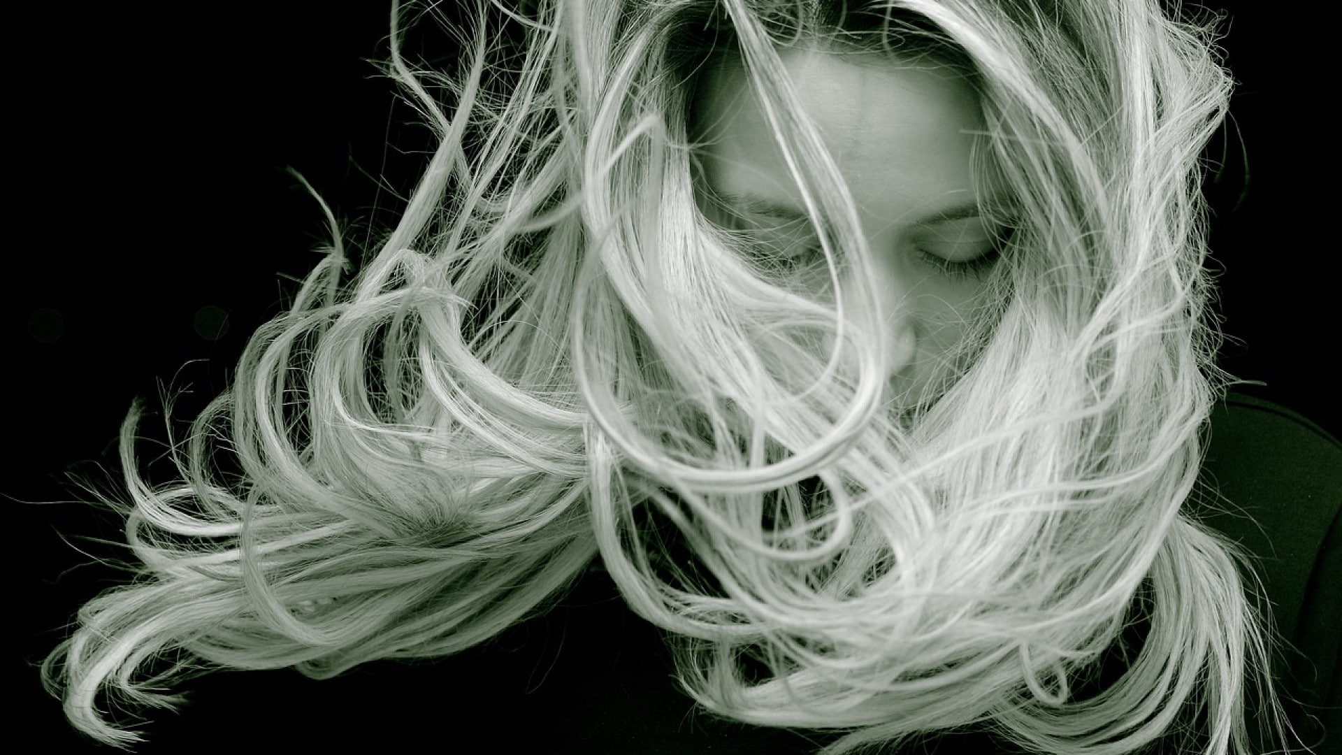 Une personne avec de longs cheveux blonds couvrant leur visage, les cheveux emportés par le vent ou en mouvement contre un fond sombre utilisent une technique