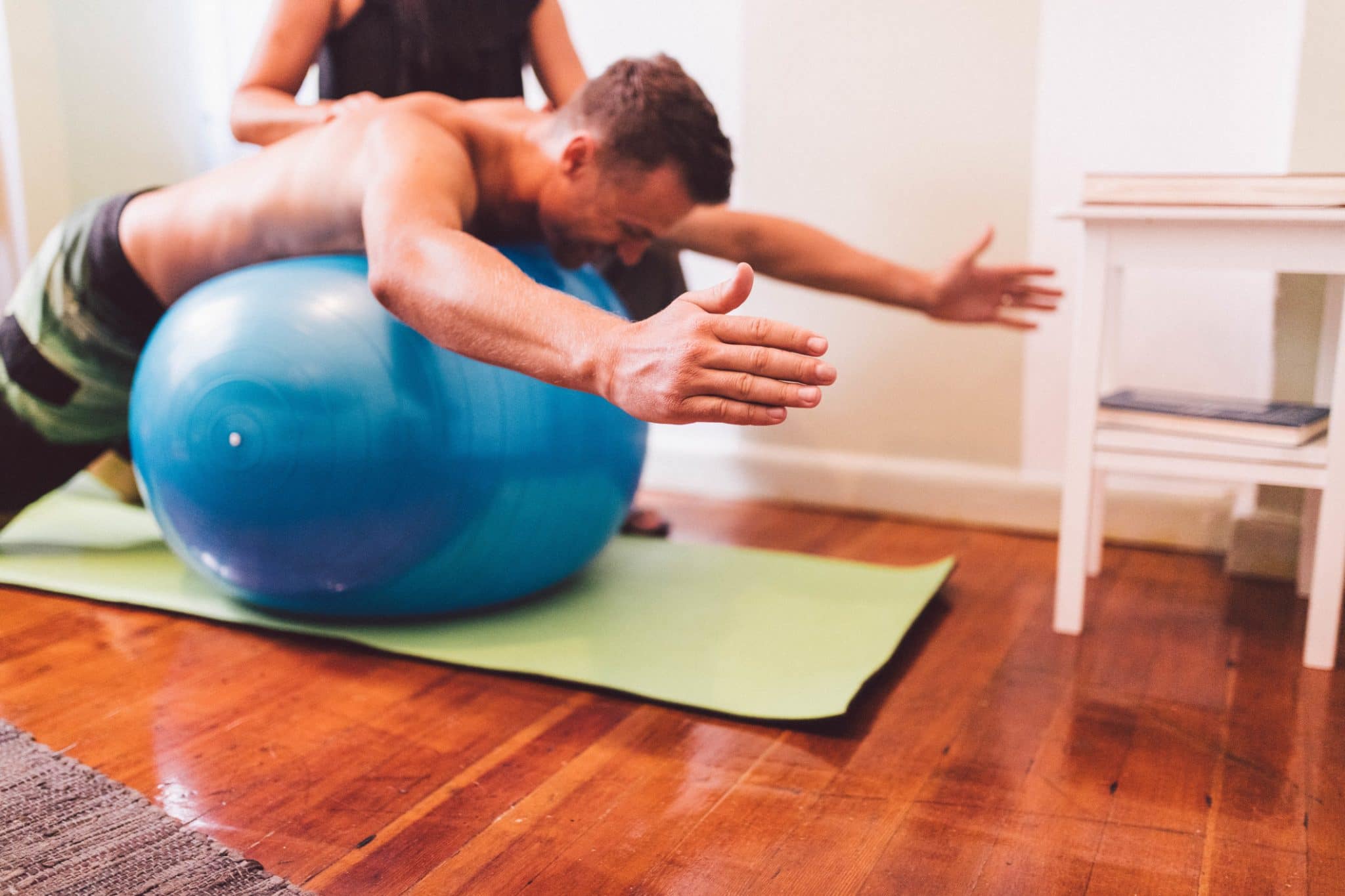 Homme effectuant un exercice d'étirement sur un tapis de yoga à l'aide d'un ballon de fitness.