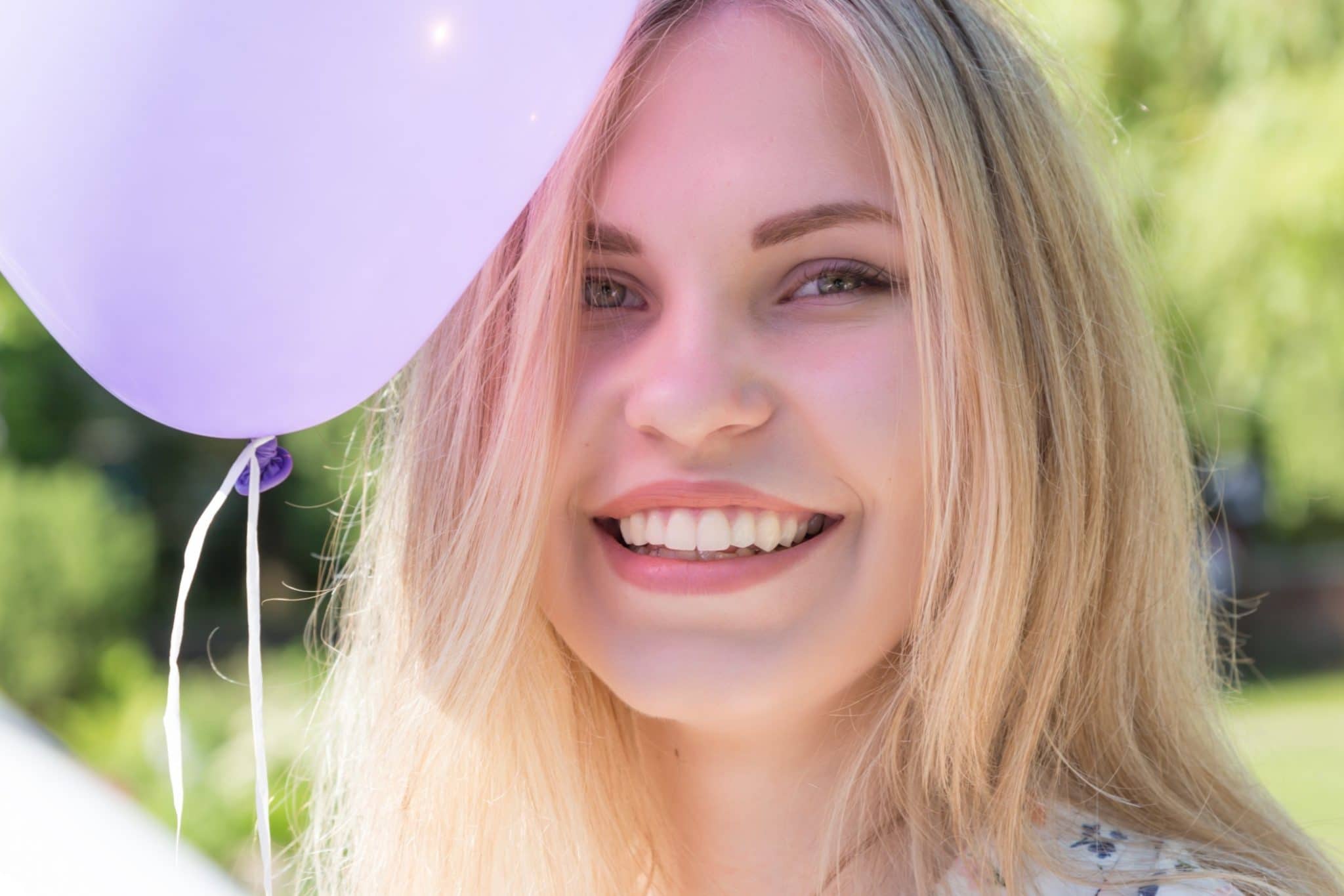 Jeune femme souriante à l'extérieur avec un ballon violet, réfléchissant à la cause de son retard à avoir ses premières règles.