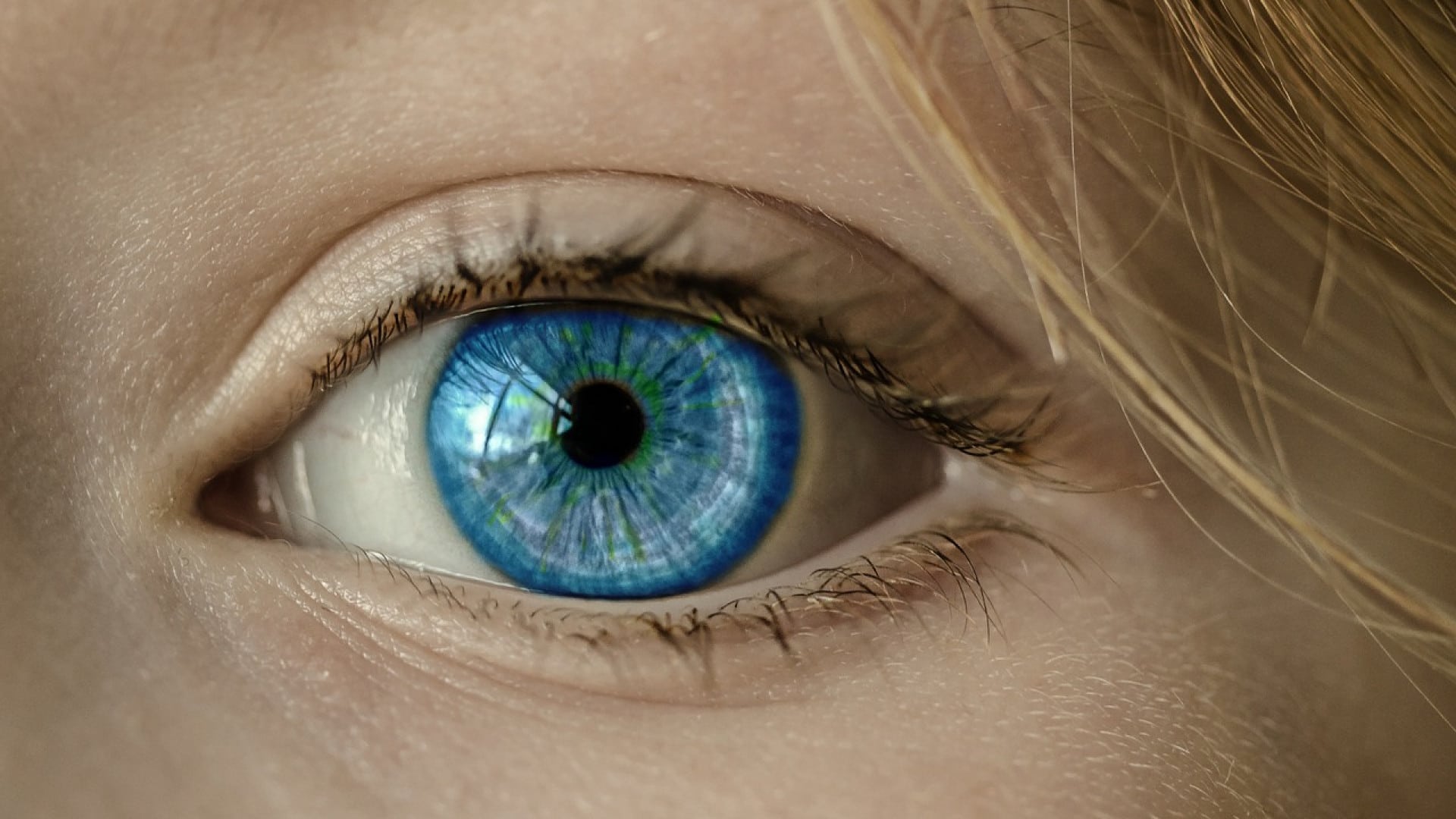 Gros plan d'un œil humain bleu avec des détails sur l'iris, les cils, la texture de la peau et les lentilles de contact visibles.
