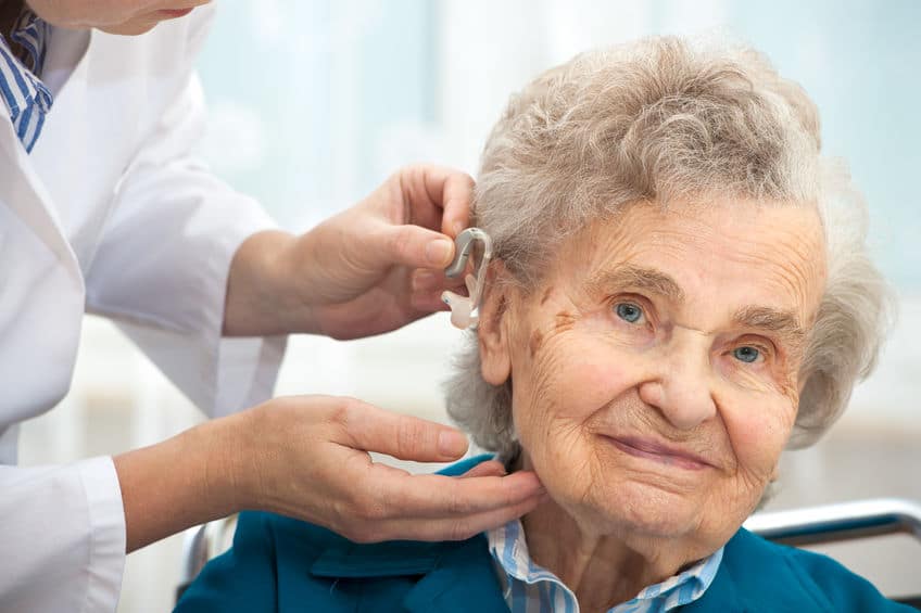 Professionnel de santé aidant une femme âgée avec son appareil auditif.