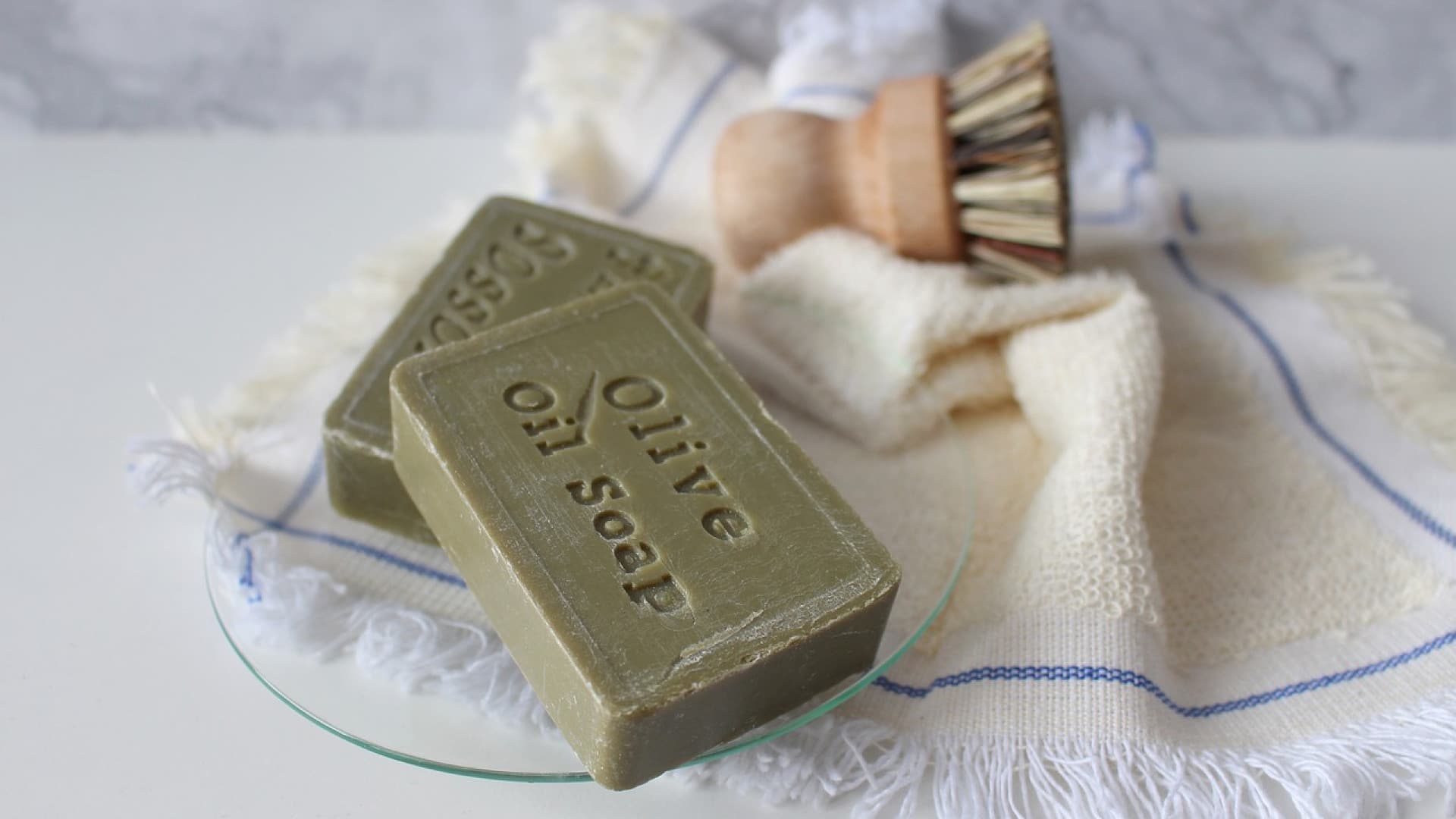 Barres de savon à l'huile d'olive avec une brosse et un gant de toilette sur une surface en marbre.