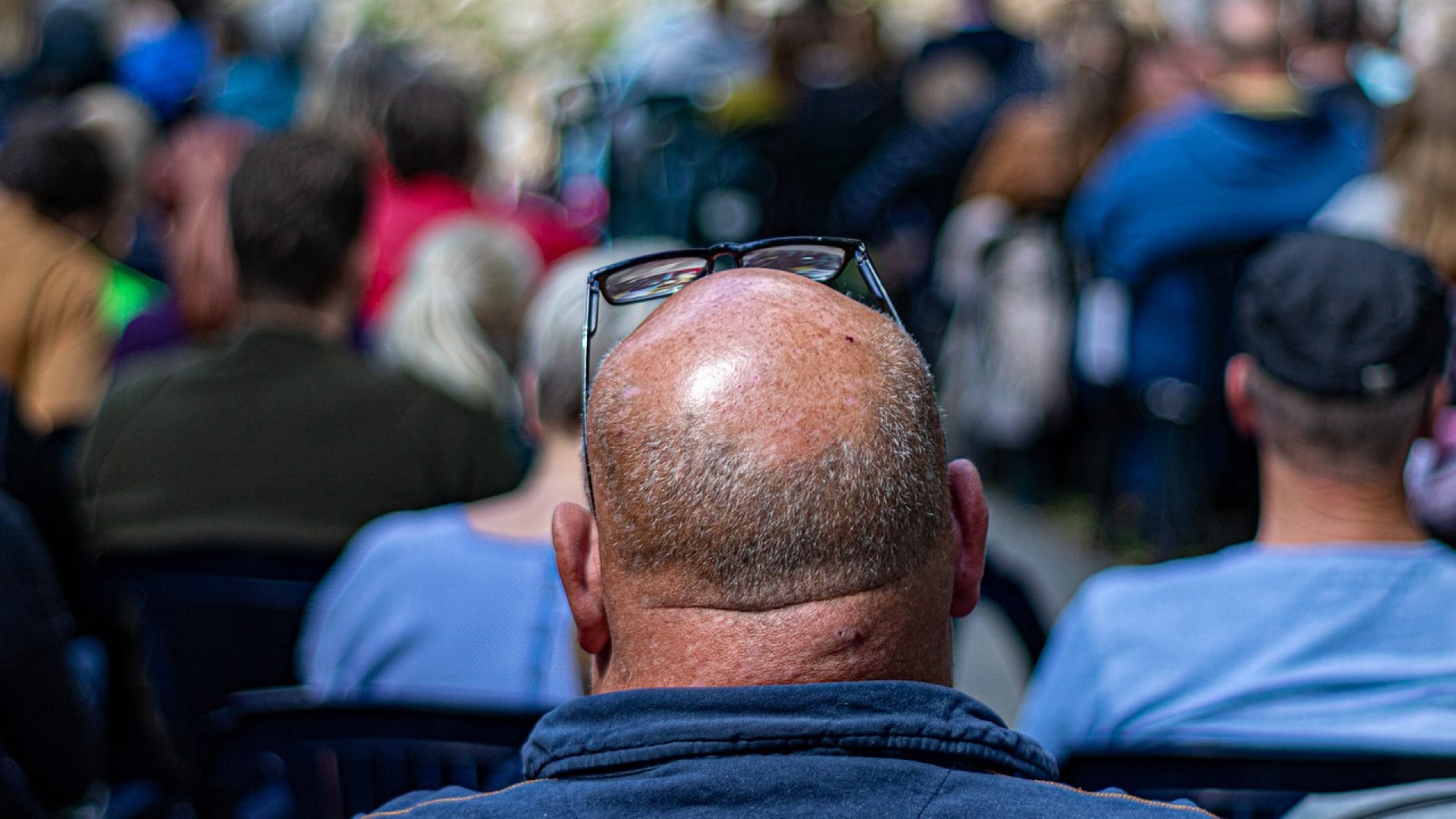Une personne atteinte d'alopécie, avec des lunettes sur la tête, assistant à un événement en plein air.