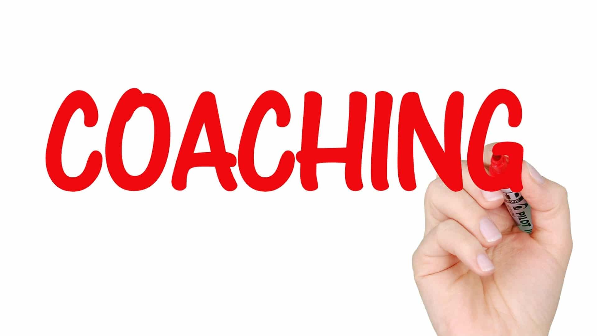 Écrire à la main le mot « coach » au marqueur rouge sur une surface claire sur un fond blanc.