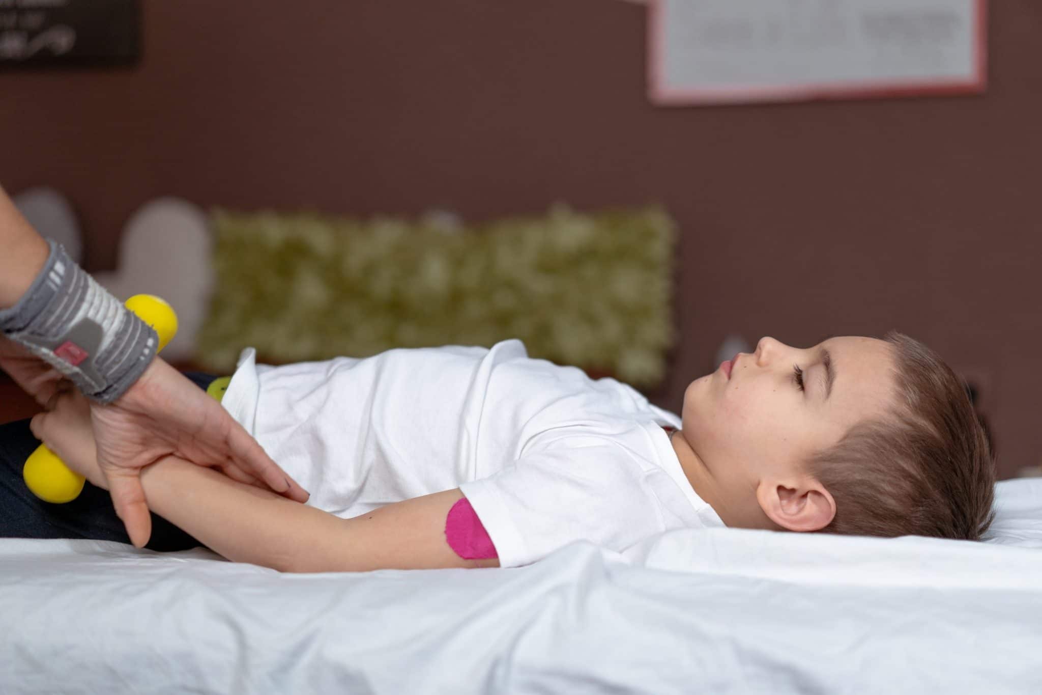 Un enfant allongé sur un lit pendant qu'un adulte tient les pieds de l'enfant avec un jouet sensoriel lors d'une séance d'ostéopathie.
