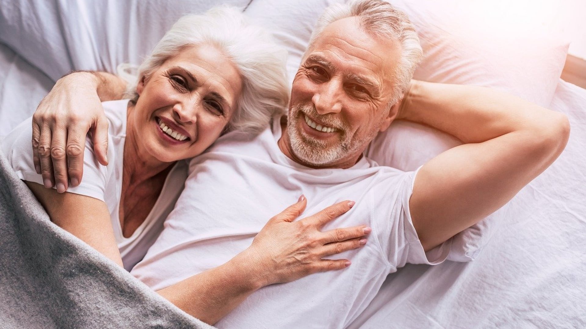 Un couple de personnes âgées souriant au lit ensemble dans leur maison de retraite médicalisée.