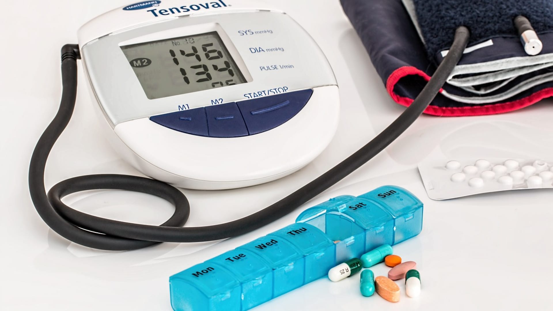 Tensiomètre électronique avec affichage des valeurs, brassard et pilulier hebdomadaire contenant divers médicaments.