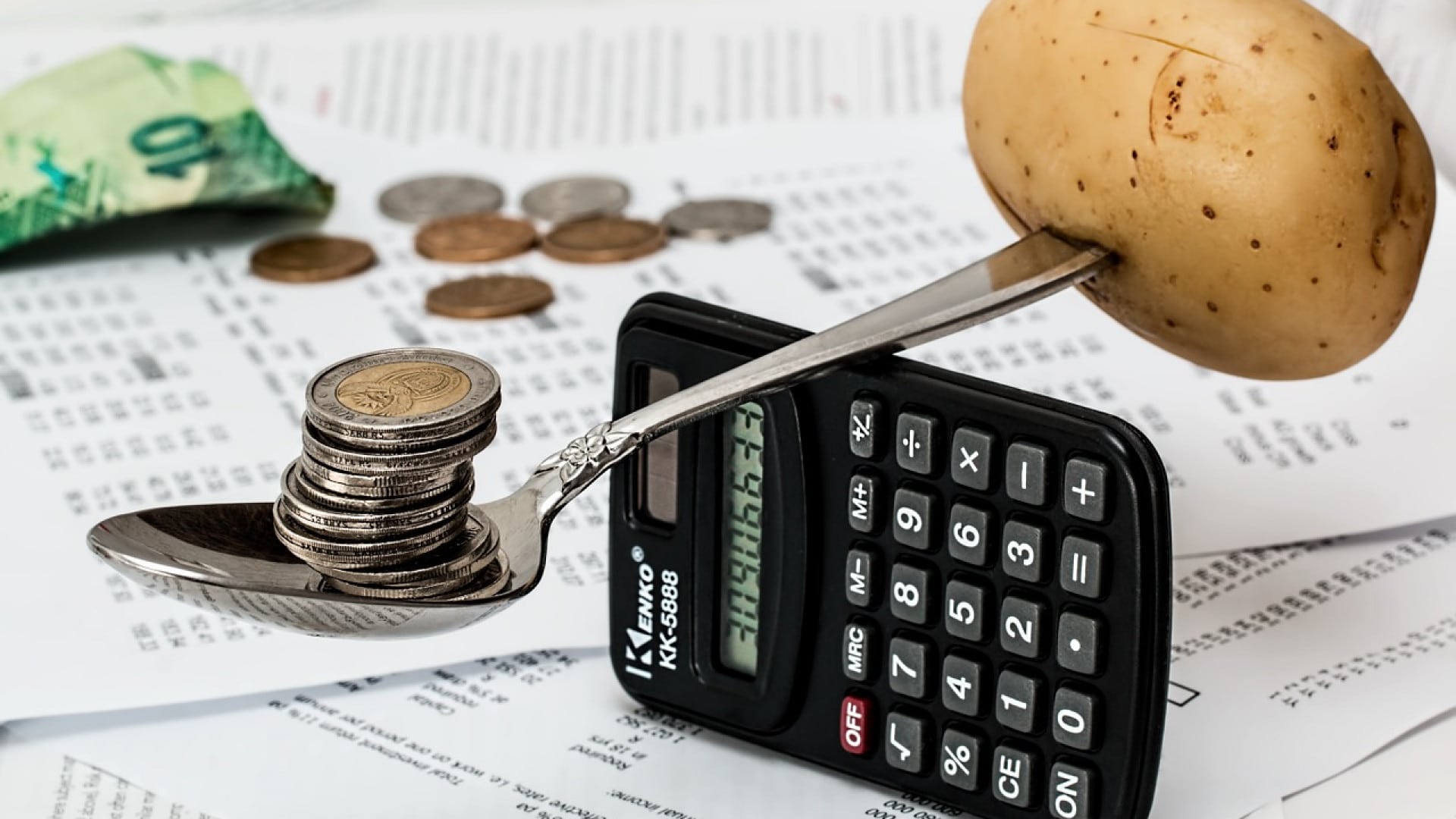 Une pomme de terre et des pièces en équilibre sur une cuillère au-dessus d'une calculatrice, symbolisant la budgétisation financière ou la comparaison des prix.