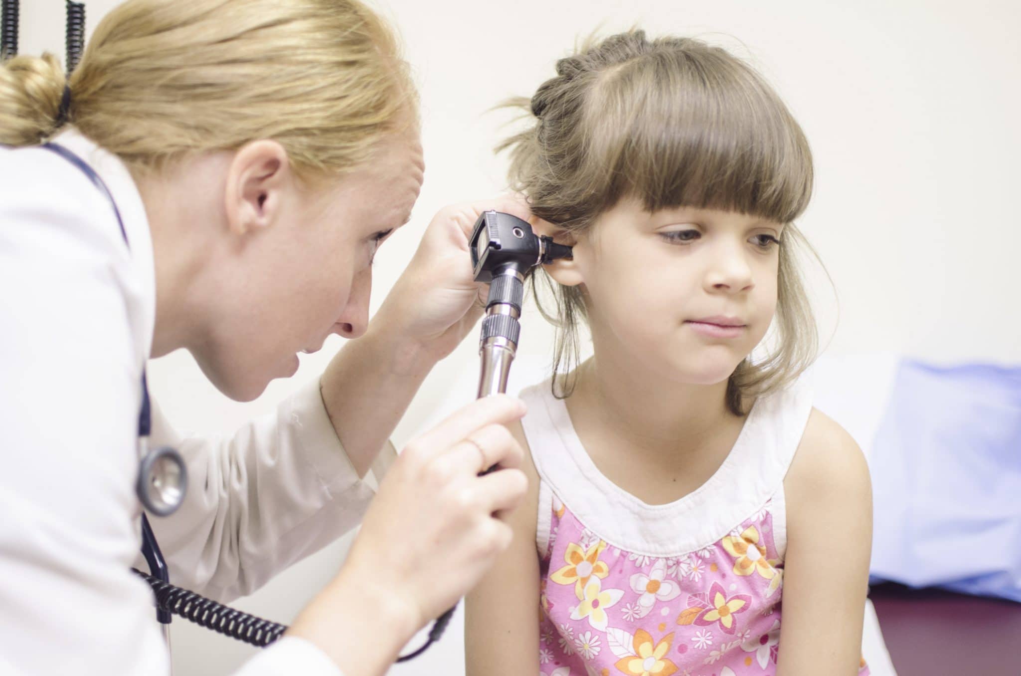 Un professionnel de la santé utilise un otoscope pour examiner l'oreille d'une jeune fille afin de déboucher une oreille.