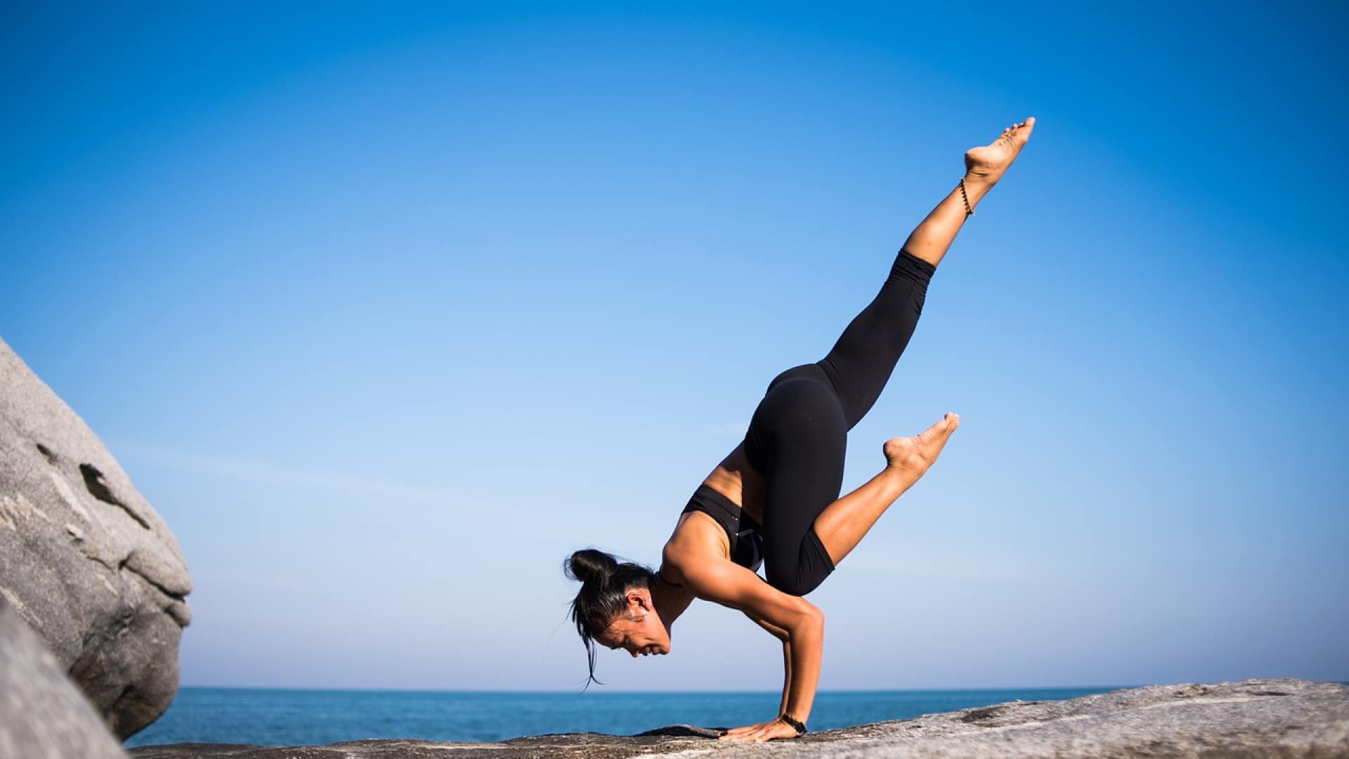 Femme pratiquant le yoga sur une côte rocheuse avec un ciel clair et la santé en arrière-plan.