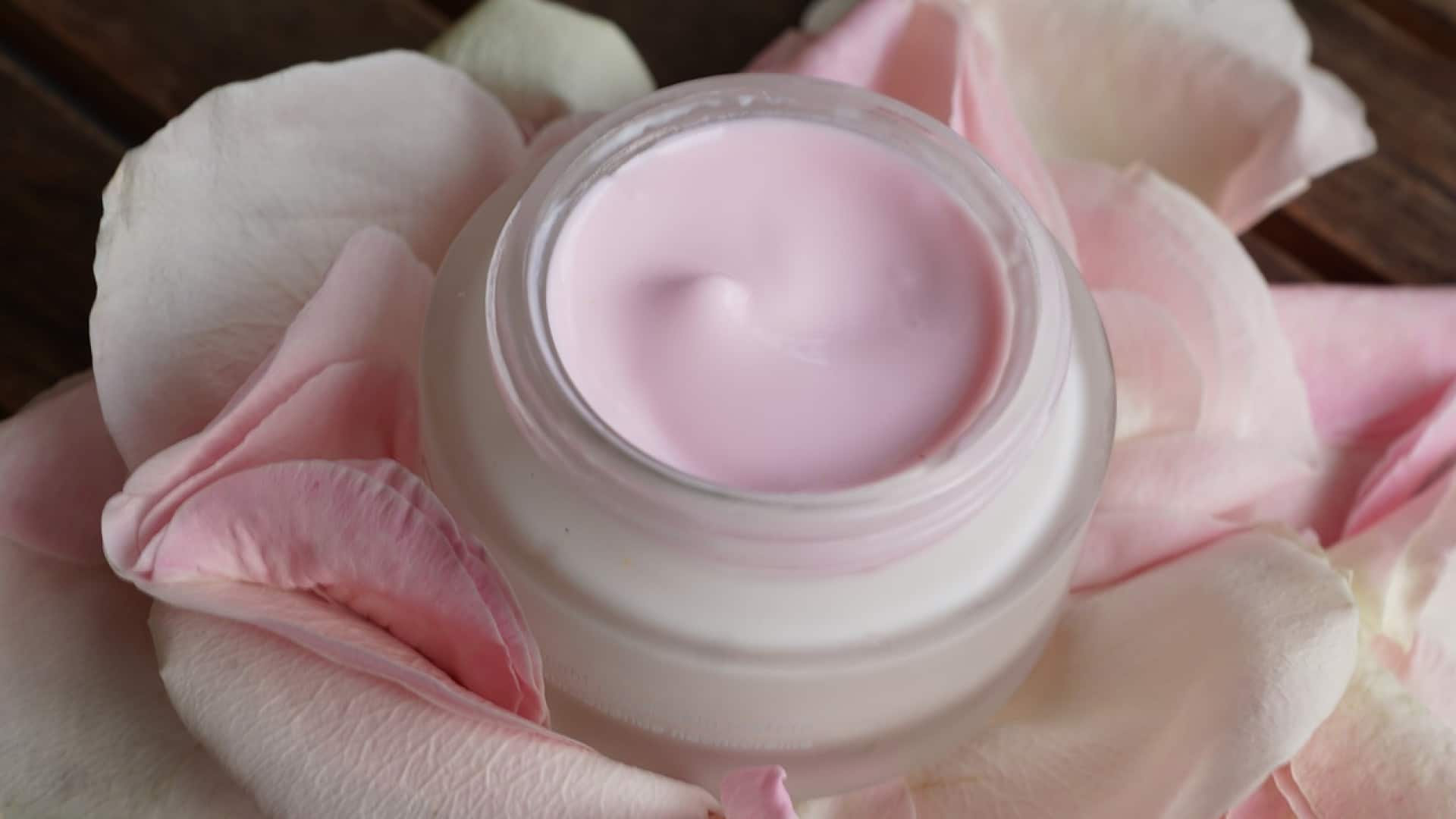 Chouchoutez votre féminité avec un pot ouvert de crème cosmétique rose entouré de pétales de roses.