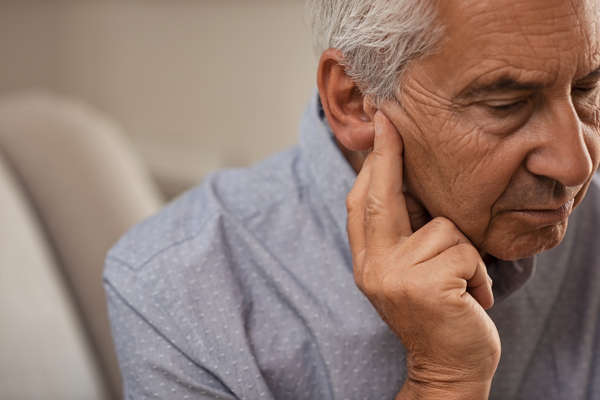 Un homme âgé semble ressentir une gêne ou une douleur à l'oreille, remarquant une boule derrière l'oreille.