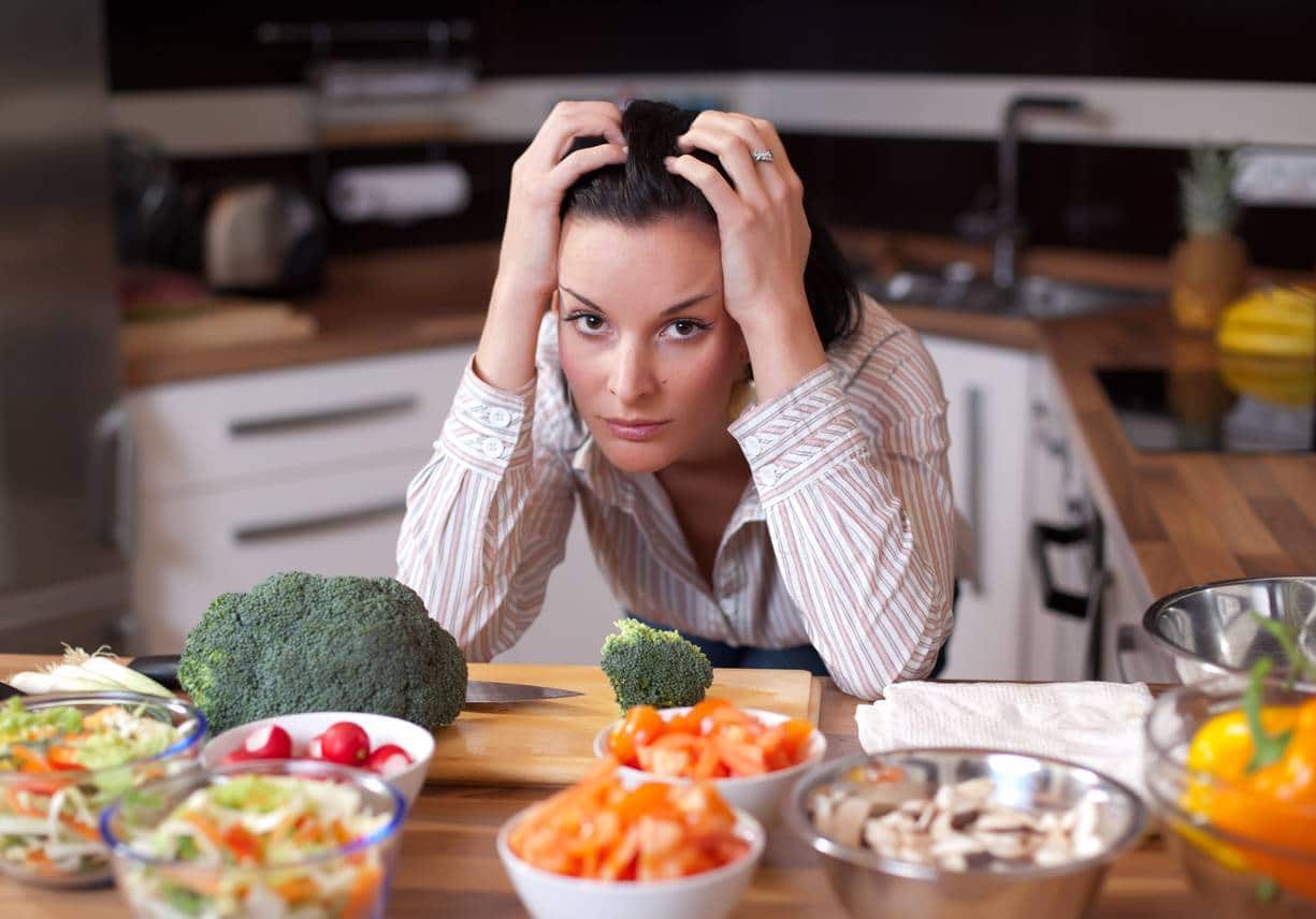 Femme ayant l'air stressée lors de la préparation de la nourriture dans la cuisine.