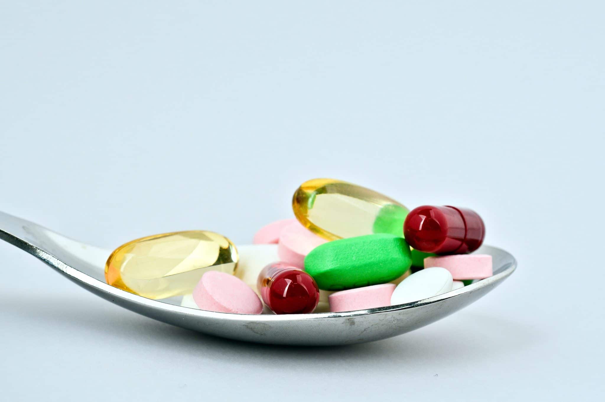 Assortiment de pilules et de capsules sur une cuillère à fond blanc, présentant une variété de compléments alimentaires disponibles.