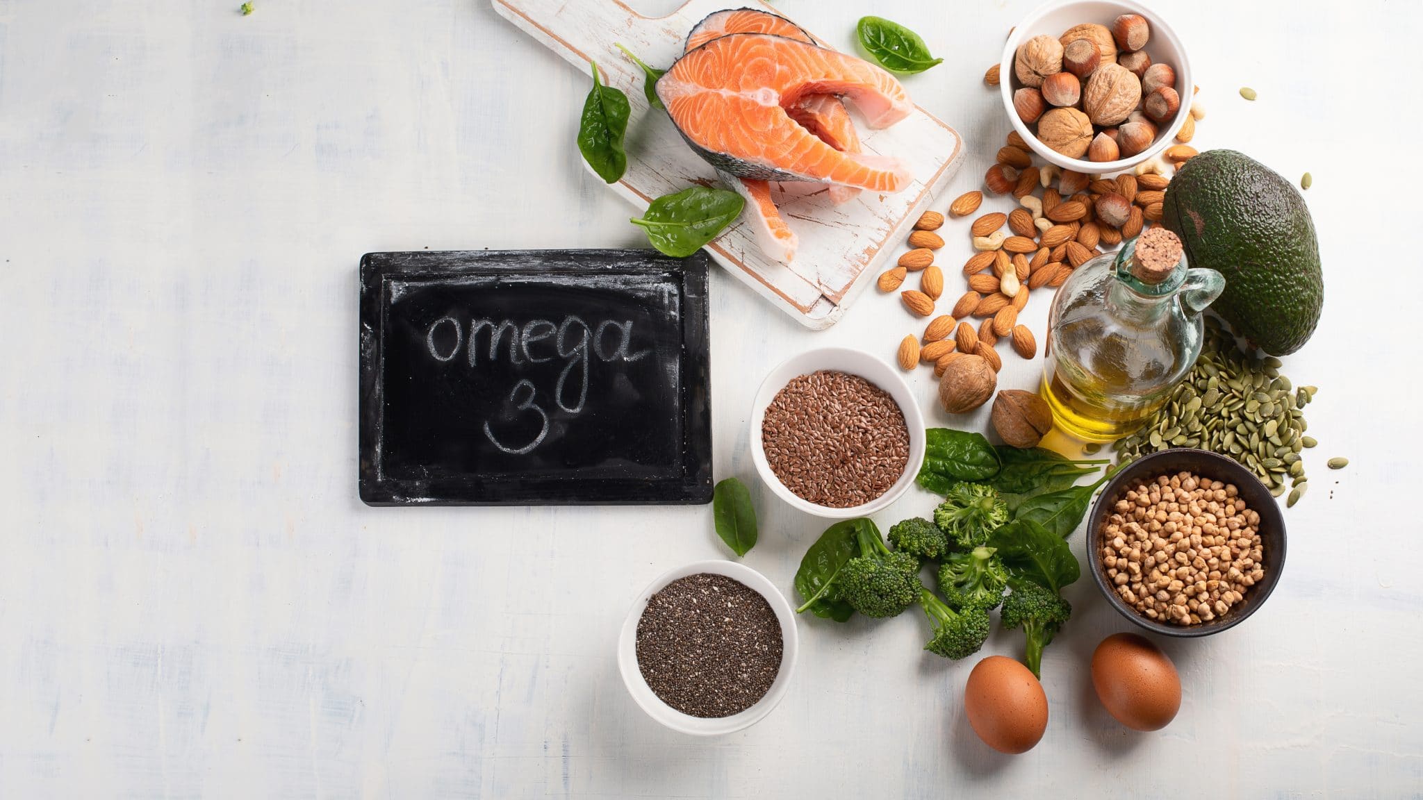 Assortiment d'aliments riches en oméga-3, notamment du poisson, des noix, des graines, des œufs et des huiles, affichés sur une surface claire avec un panneau indiquant « oméga 3 ».