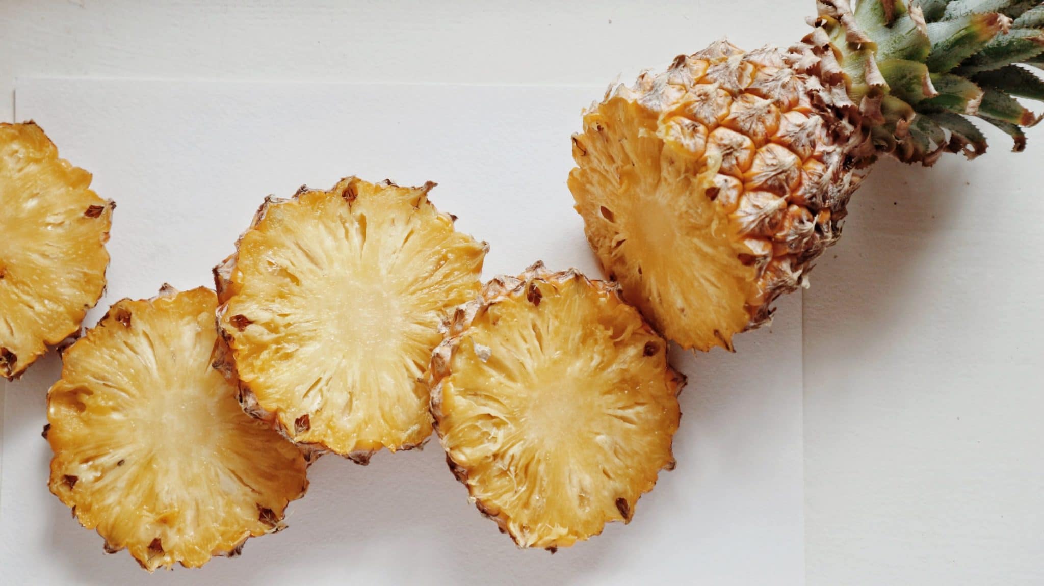 Morceaux d'ananas tranchés disposés à côté d'un ananas entier sur une surface claire.