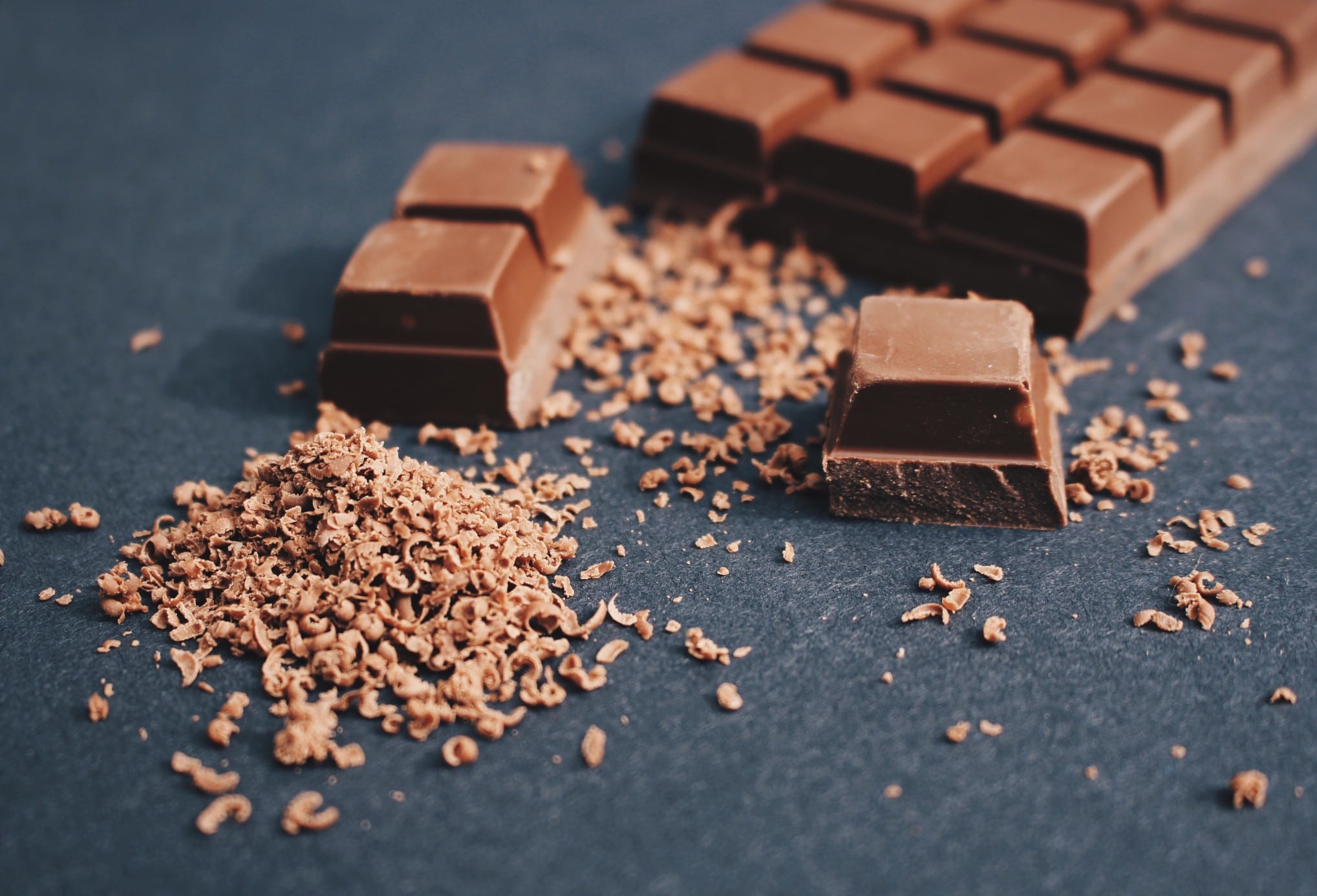Une barre de chocolat avec un morceau cassé, entourée de copeaux de chocolat sur une surface sombre, éveille l'envie.