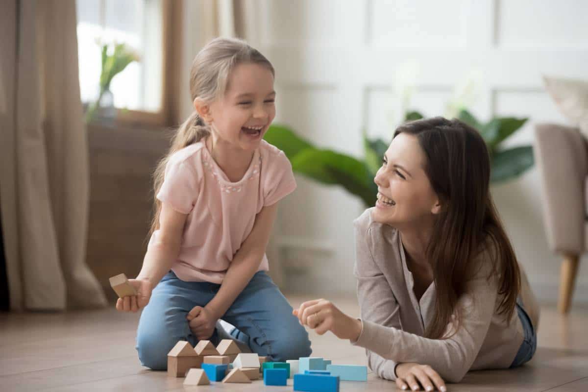 Une femme et une jeune fille rient ensemble en jouant avec des blocs au sol, profitant du moment en toute la famille.