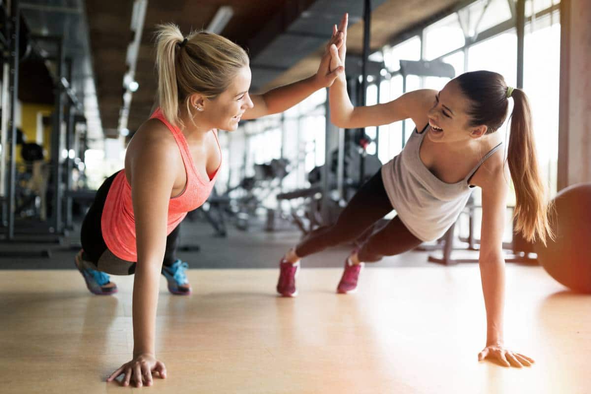 Deux femmes se retrouvent à faire des pompes et se donnent un high-five dans une salle de gym, cherchant à retrouver la forme.