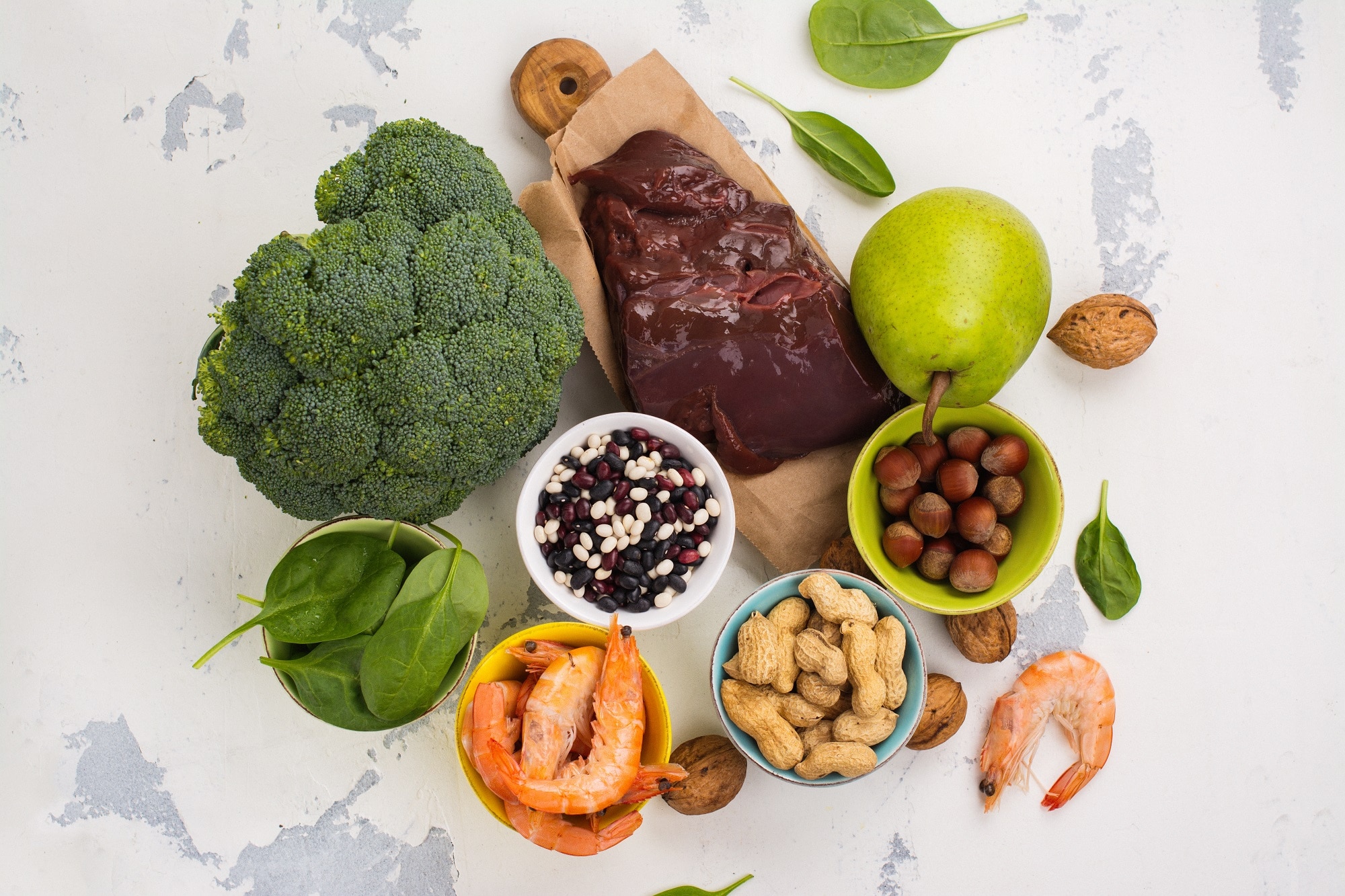 Divers aliments sains, notamment des fruits, des légumes, des noix, des crevettes et du foie riches en vitamine B9 sur une surface légère.