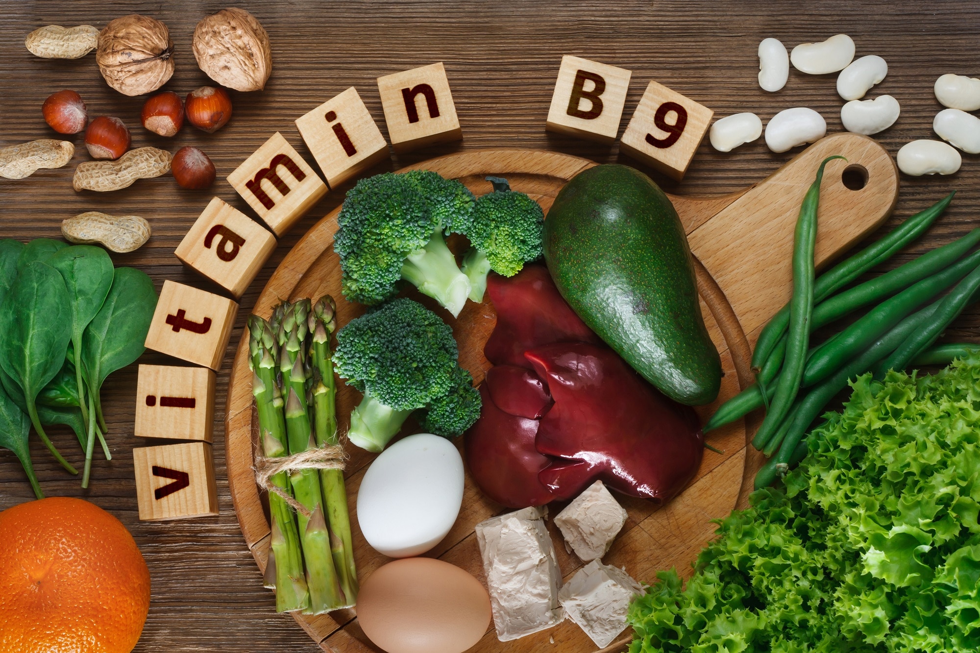 Aliments assortis riches en vitamine B9 (folate) présentés avec une étiquette inscrite dans des blocs de bois, illustrant le savoir-faire nécessaire pour traiter la carence en vitamine B9.