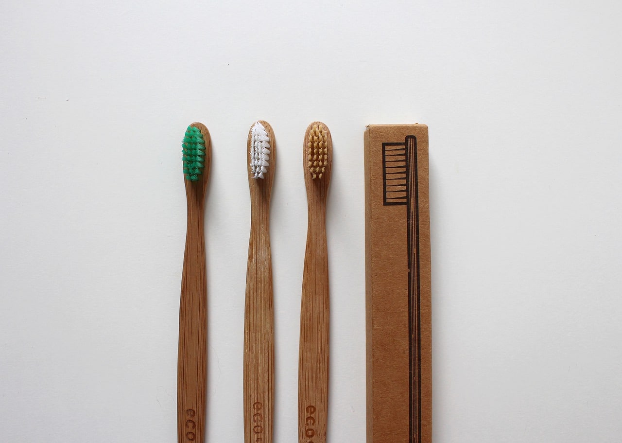 Trois brosses à dents en bambou et une règle en bois placées en rangée sur une surface blanche.