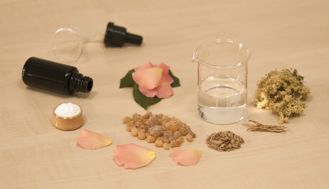 Ingrédients d'aromathérapie sur une surface en bois, comprenant de l'huile essentielle, un bécher en verre, des pétales de rose, des herbes et des cristaux.