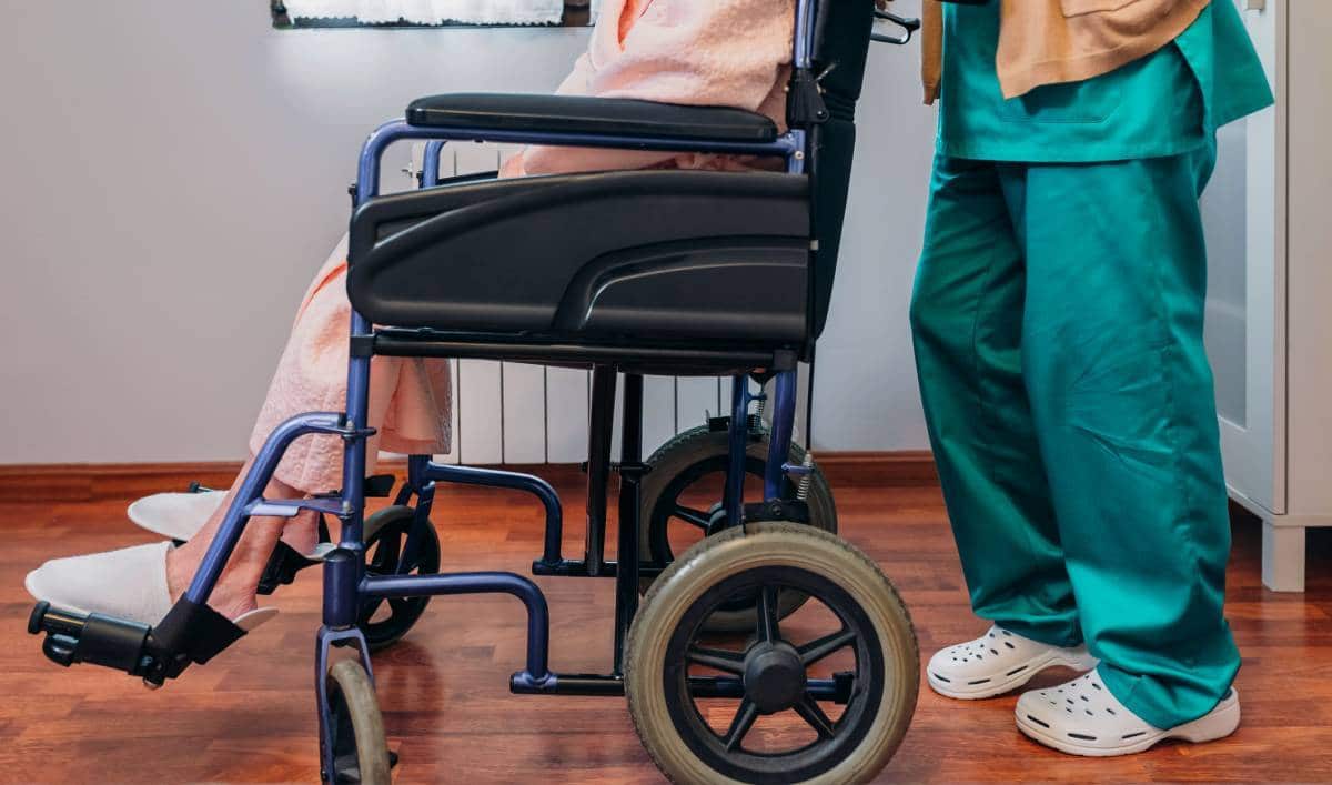 Professionnel de la santé debout à côté d’un patient en fauteuil roulant.