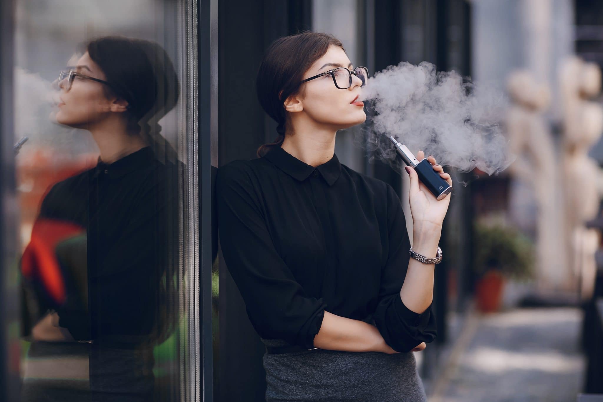 Jeune femme exhalant la vapeur d’une cigarette électronique Eleaf iStick TC 40 W alors qu’elle se tenait près d’une vitre.