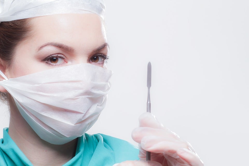 Un professionnel de la santé portant un masque chirurgical et une casquette tient un scalpel, prêt pour une intervention de chirurgie esthétique.