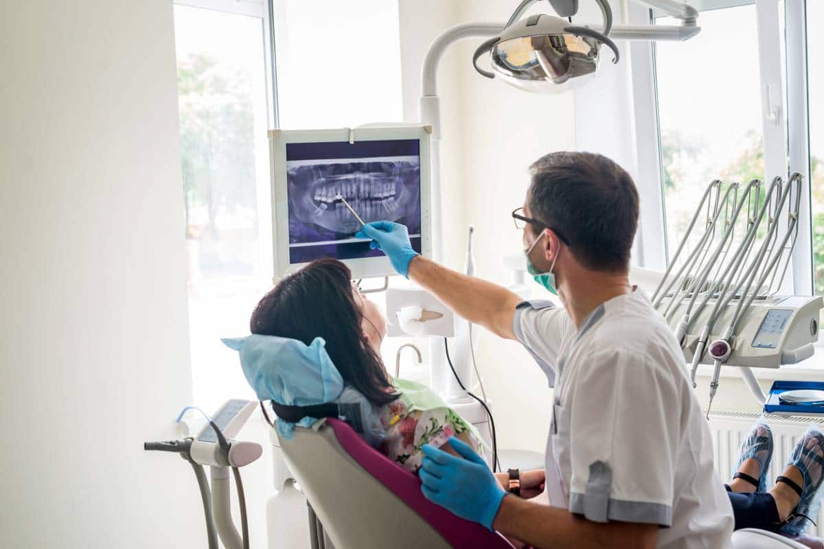 Dentiste examinant des images radiographiques avec un patient dans une clinique dentaire, discutant des évolutions en Radiologie dentaire.