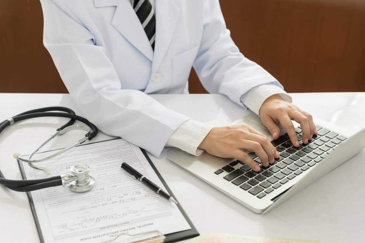 Un médecin tapant sur un ordinateur portable avec un stéthoscope et des documents médicaux sur le bureau.