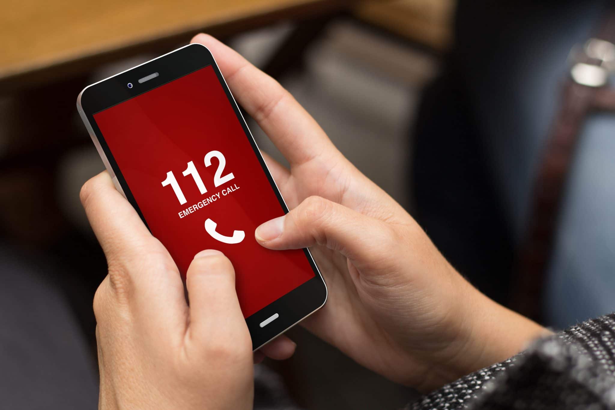 Une personne tient entre ses mains un smartphone affichant une liste de numéros d'urgence sur l'écran, dont le « 112 ».