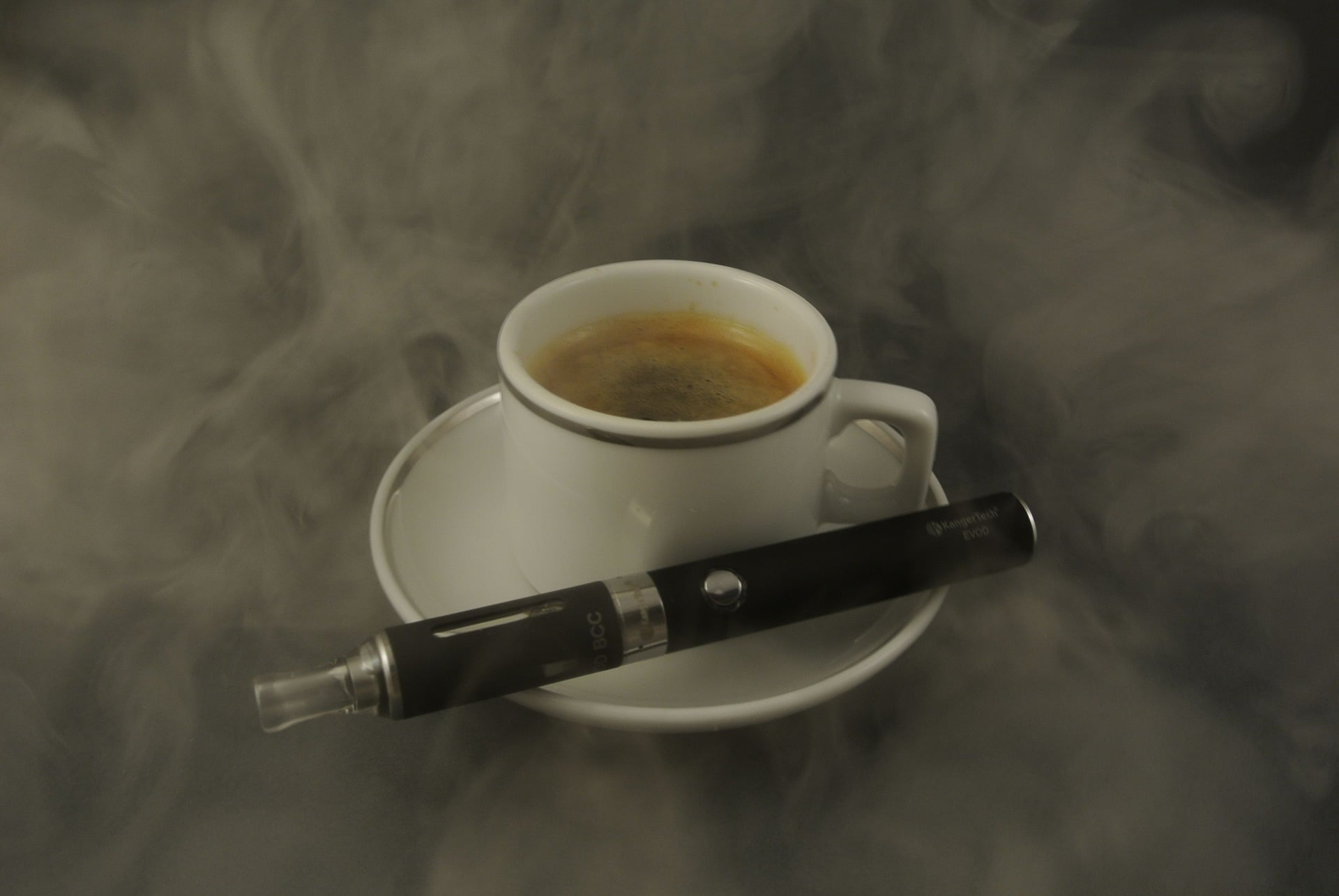 Une tasse de café entourée de vapeur et une cigarette électronique conçue pour aider les fumeurs posée à côté d'elle sur la soucoupe.