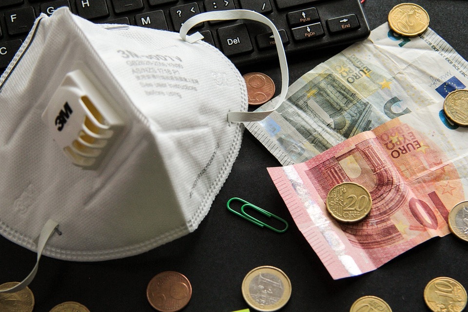 Masque protecteur sur un clavier d'ordinateur portable avec une monnaie européenne dispersée, symbolisant pourquoi souscrire à une assurance maladie complémentaire.