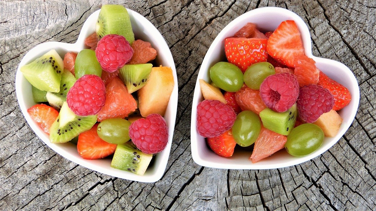 Deux corbeilles de fruits en forme de coeur remplies de fruits frais assortis sur une surface en bois.