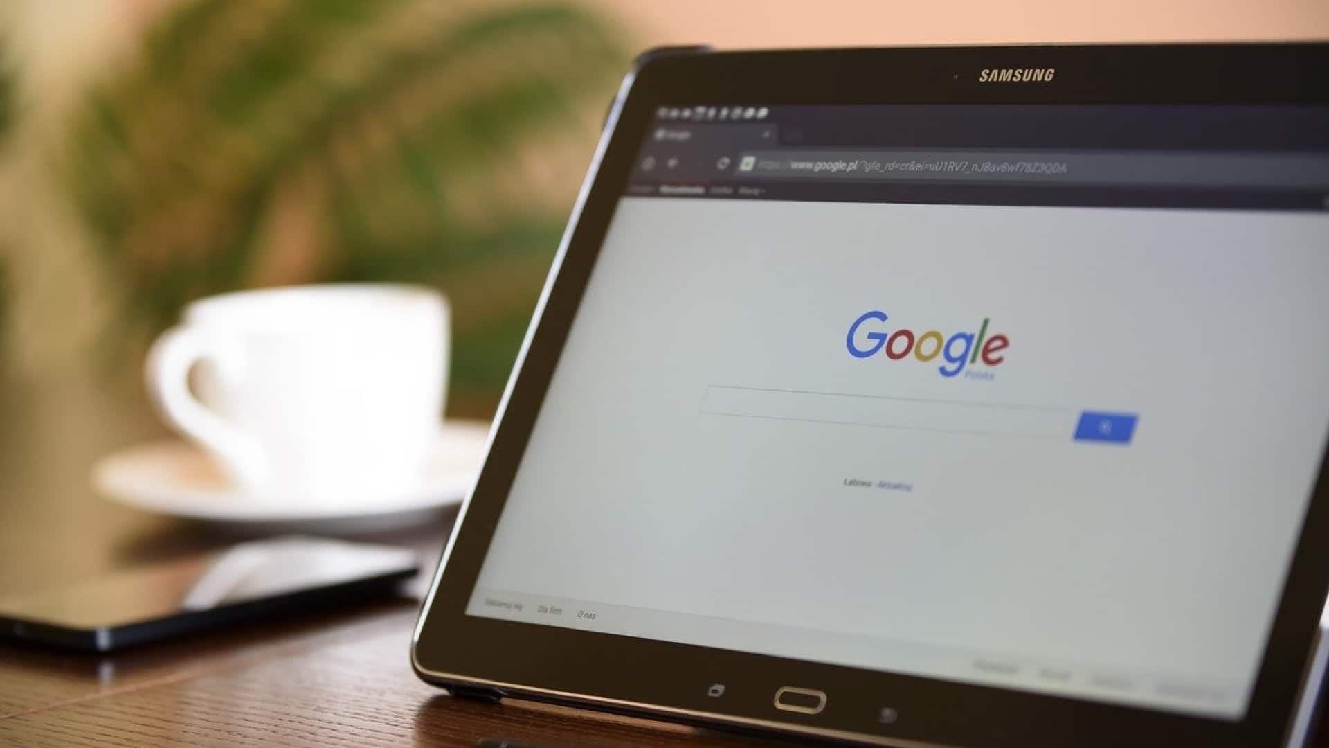 Une tablette Samsung affichant la page d'accueil de Google et les codes promotionnels sur une table en bois à côté d'une tasse blanche.