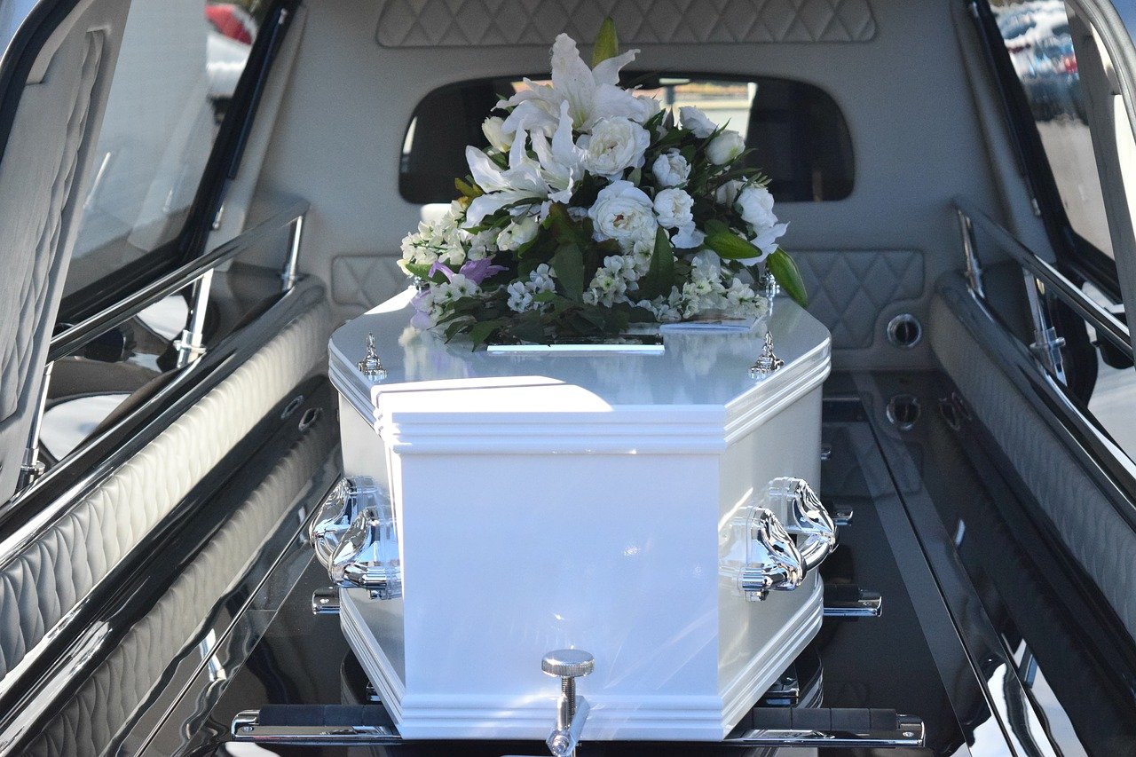 Coffret blanc orné de fleurs à l'intérieur d'un corbillard, mettant en valeur les essentiels de l'assurance obsèques.